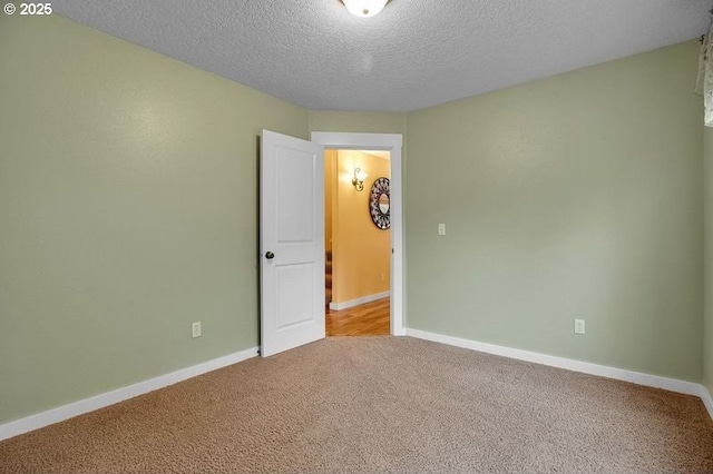 carpeted spare room featuring a textured ceiling and baseboards