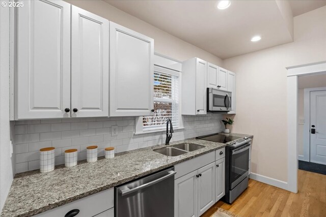 kitchen featuring sink, light stone countertops, light wood-type flooring, white cabinetry, and stainless steel appliances