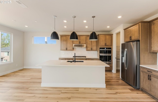 17437 NW Antonio St, Portland, OR 97229 - kitchen featuring appliances with stainless steel finishes, a kitchen island with sink, decorative backsplash, light countertops, and brown cabinetry
