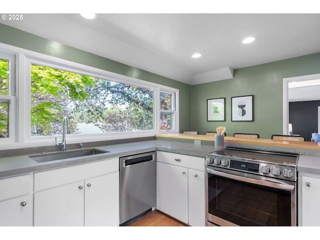 kitchen with a sink, white cabinets, stainless steel appliances, recessed lighting, and light wood-style flooring