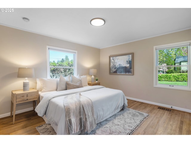bedroom featuring baseboards, visible vents, ornamental molding, and wood finished floors