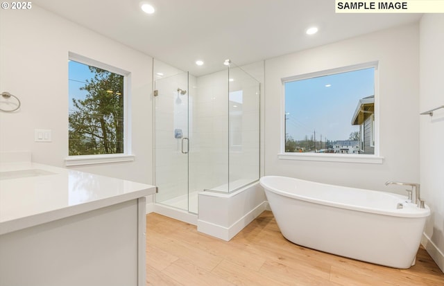 bathroom with wood finished floors, a shower stall, a soaking tub, recessed lighting, and vanity