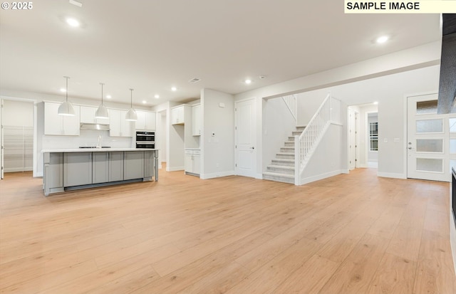 unfurnished living room with stairs, light wood-style flooring, baseboards, recessed lighting, and a sink