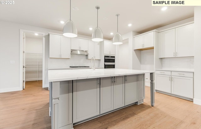 kitchen with under cabinet range hood, black appliances, tasteful backsplash, light wood-style flooring, and recessed lighting