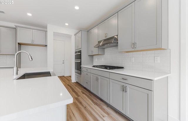 27226 SW Yarrow Ln, Wilsonville, OR 97070 - kitchen with under cabinet range hood, a sink, gray cabinetry, stainless steel appliances, and light wood-style flooring