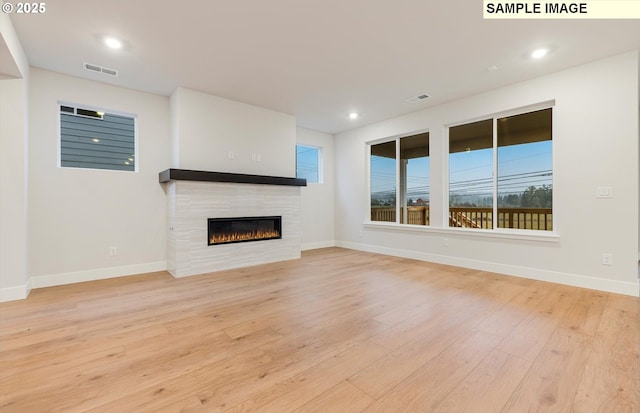 unfurnished living room with light wood-style flooring, a fireplace, baseboards, and recessed lighting