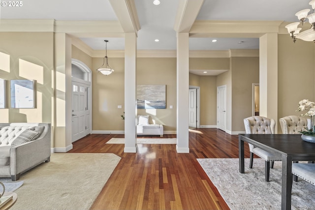 entrance foyer with ornate columns, crown molding, dark hardwood / wood-style floors, and an inviting chandelier