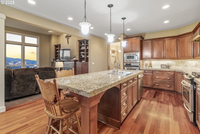 kitchen with sink, a breakfast bar area, a kitchen island with sink, stainless steel appliances, and light wood-type flooring