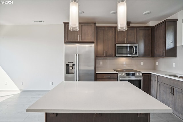 kitchen with stainless steel appliances, backsplash, dark brown cabinets, hanging light fixtures, and a kitchen island