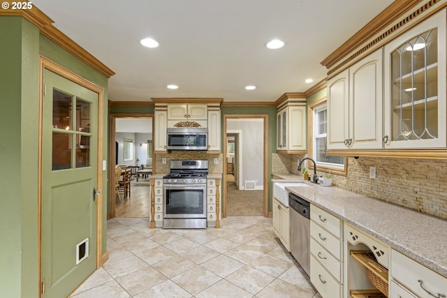 kitchen featuring stainless steel appliances, a sink, light tile patterned floors, backsplash, and crown molding