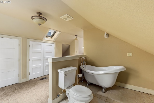 full bath with lofted ceiling, toilet, a freestanding bath, baseboards, and a skylight