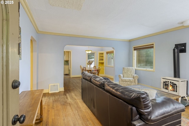 living area with arched walkways, light wood finished floors, ornamental molding, a wood stove, and a textured ceiling