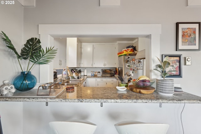 kitchen featuring white cabinetry, sink, light stone counters, and stainless steel refrigerator