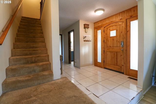 entrance foyer featuring light tile patterned floors, a textured ceiling, and wood walls