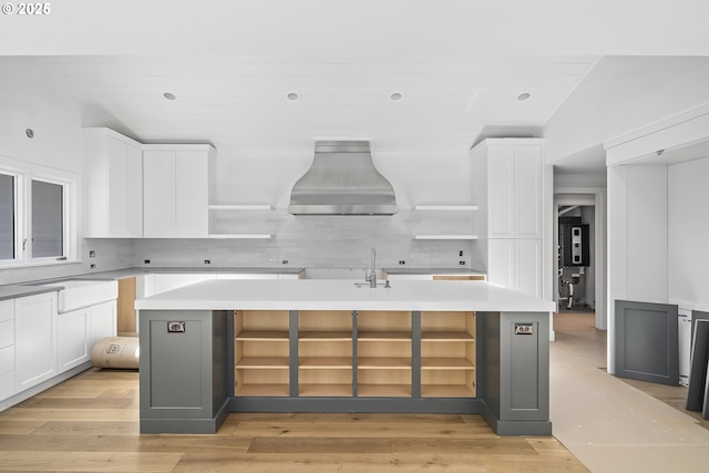 12643 S Iron Mountain Blvd, Portland, OR 97219 - kitchen featuring open shelves, wall chimney exhaust hood, white cabinetry, an island with sink, and backsplash