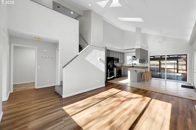 unfurnished living room featuring hardwood / wood-style flooring, high vaulted ceiling, ceiling fan, and a skylight