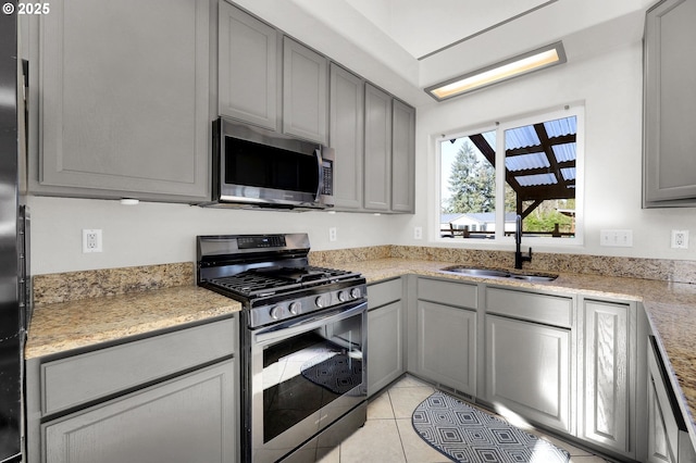 kitchen featuring sink, light tile patterned floors, gray cabinets, appliances with stainless steel finishes, and light stone countertops