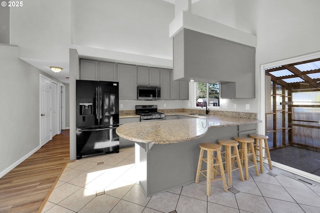 kitchen featuring appliances with stainless steel finishes, sink, gray cabinetry, a kitchen bar, and kitchen peninsula