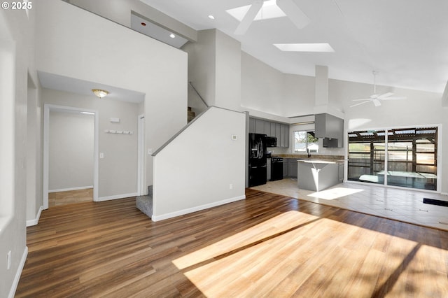 unfurnished living room featuring wood-type flooring, a skylight, high vaulted ceiling, and ceiling fan