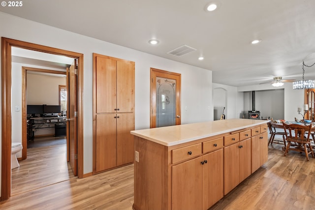kitchen with a wood stove, light wood-style flooring, visible vents, recessed lighting, and a kitchen island