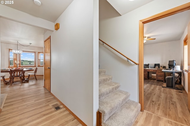 stairs featuring visible vents, baseboards, a notable chandelier, and wood finished floors