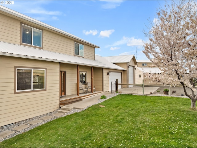 back of house with driveway, an attached garage, metal roof, and a lawn