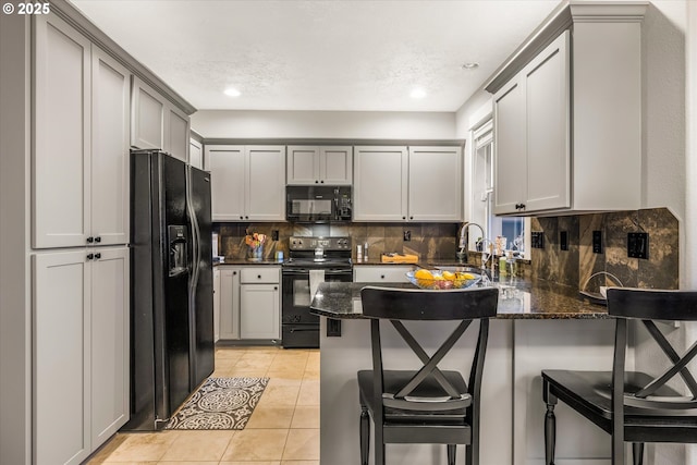 kitchen with dark stone countertops, a breakfast bar, a sink, and black appliances