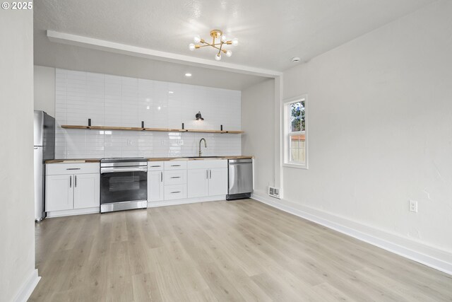 1061 NE Avery St, Newport, OR 97365 - kitchen with stainless steel appliances, a sink, open shelves, backsplash, and light wood-type flooring