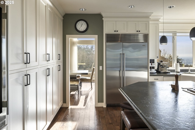 kitchen featuring a breakfast bar, decorative light fixtures, dark hardwood / wood-style flooring, built in refrigerator, and crown molding