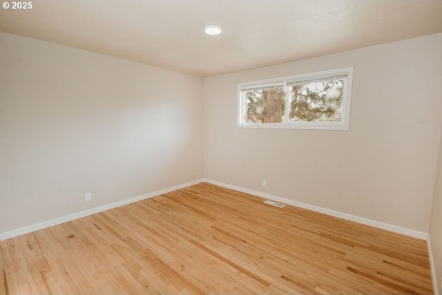 empty room featuring wood finished floors, visible vents, and baseboards