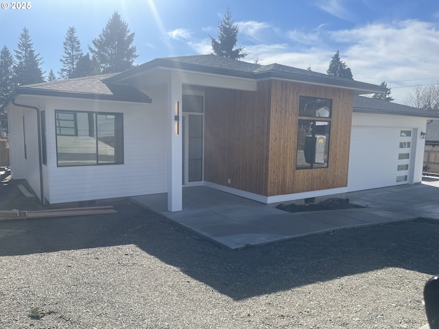 view of side of home featuring an attached garage, driveway, and roof with shingles