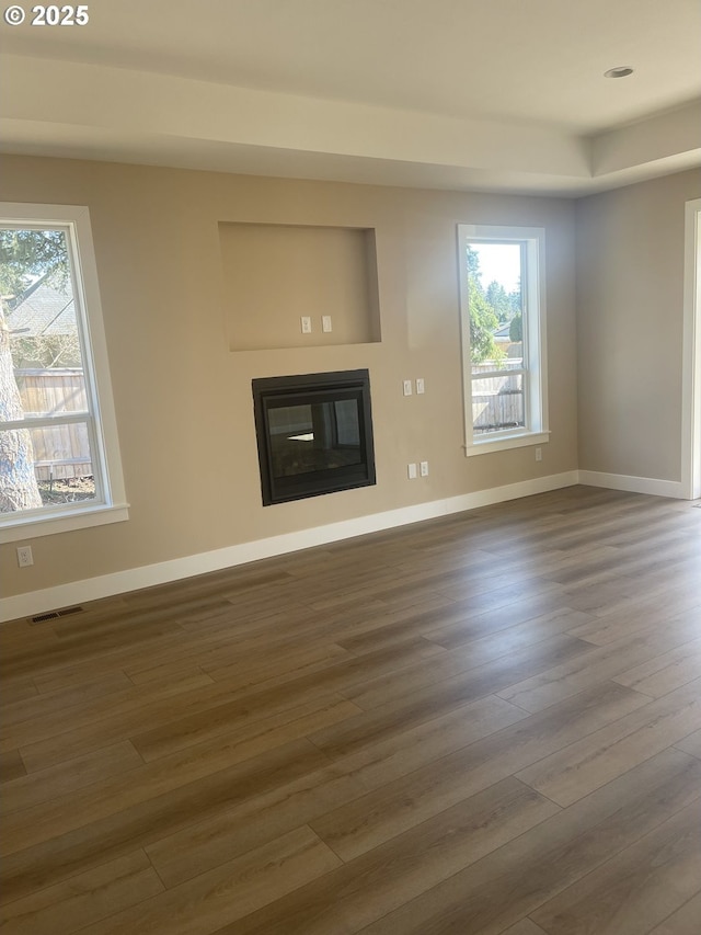 unfurnished living room featuring wood finished floors, a glass covered fireplace, visible vents, and a healthy amount of sunlight