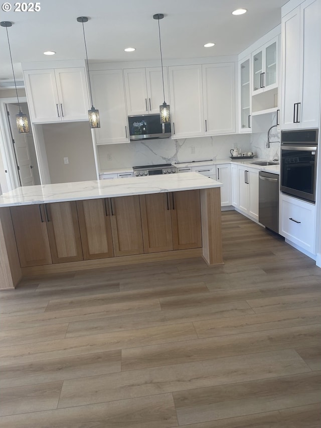 kitchen featuring stainless steel appliances, a sink, white cabinets, light wood-type flooring, and a center island