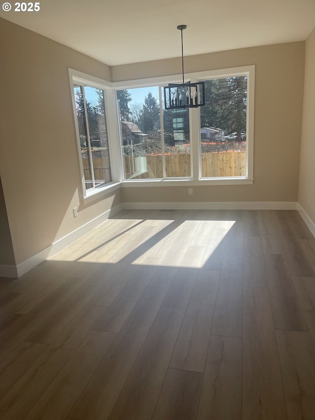 unfurnished dining area featuring baseboards, a chandelier, and wood finished floors