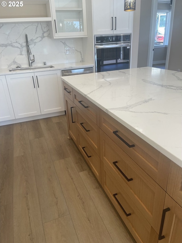 kitchen featuring white cabinets, light stone counters, oven, and light wood-style floors