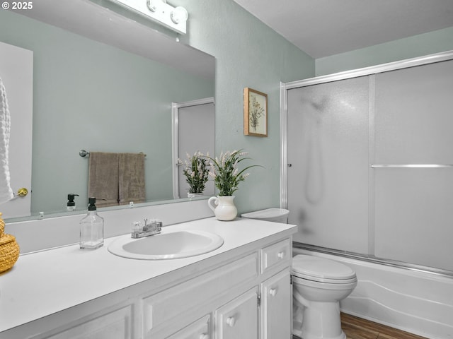 full bathroom featuring vanity, hardwood / wood-style flooring, toilet, and combined bath / shower with glass door