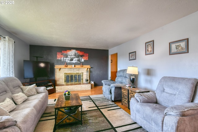 living area featuring a brick fireplace, a textured ceiling, an accent wall, and wood finished floors