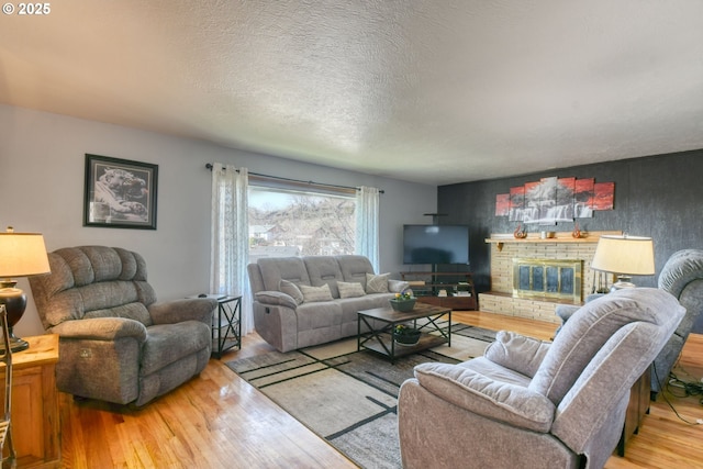 living area featuring an accent wall, a brick fireplace, a textured ceiling, and wood finished floors