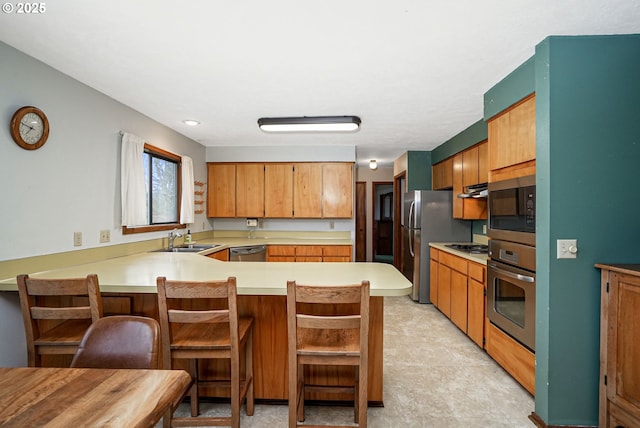 kitchen with a breakfast bar, light countertops, appliances with stainless steel finishes, a sink, and a peninsula