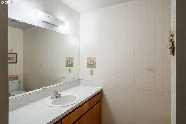 half bath with vanity, toilet, and wallpapered walls