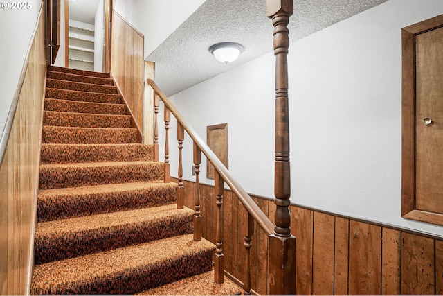 staircase with a textured ceiling, wood walls, and wainscoting