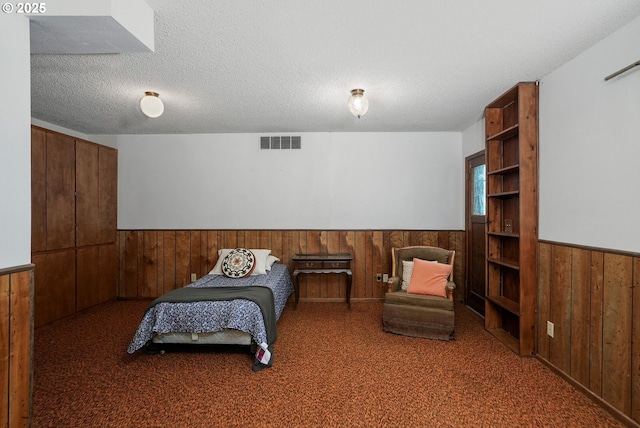 bedroom featuring a textured ceiling, wooden walls, a wainscoted wall, carpet floors, and visible vents