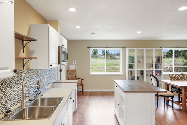 kitchen with a sink, light wood-type flooring, open shelves, tasteful backsplash, and stainless steel microwave