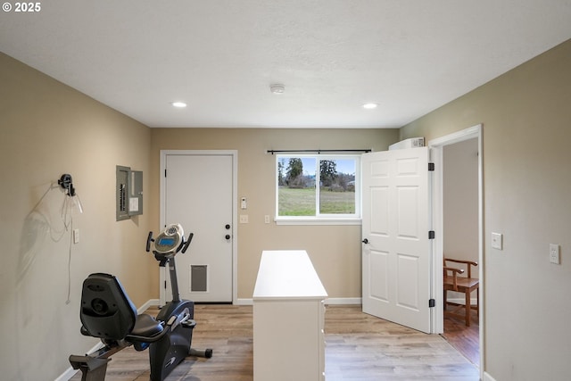 workout area featuring light wood-style floors, recessed lighting, electric panel, and baseboards