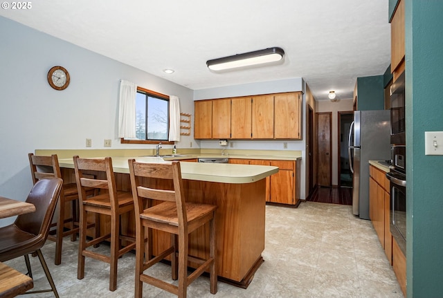 kitchen with brown cabinets, a breakfast bar area, light countertops, appliances with stainless steel finishes, and a peninsula