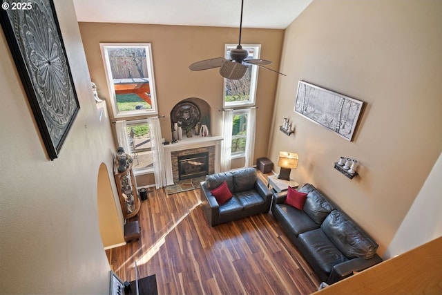 living room featuring ceiling fan, a fireplace, dark hardwood / wood-style flooring, and a high ceiling