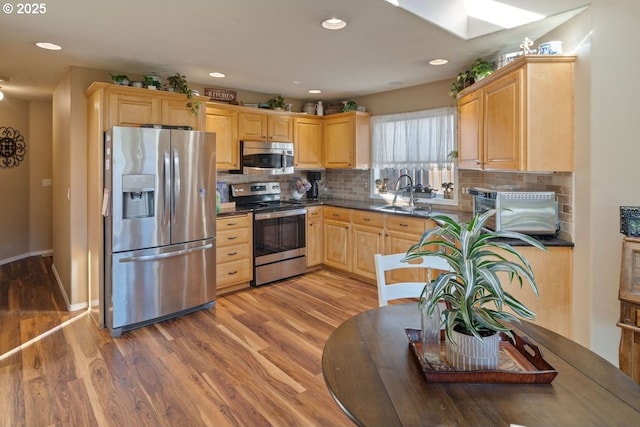 kitchen featuring appliances with stainless steel finishes, hardwood / wood-style floors, light brown cabinetry, sink, and backsplash