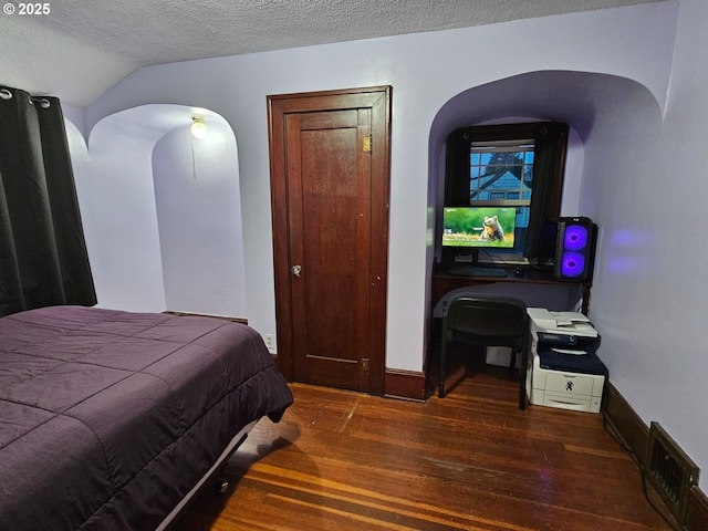 bedroom with vaulted ceiling, a textured ceiling, and dark hardwood / wood-style flooring