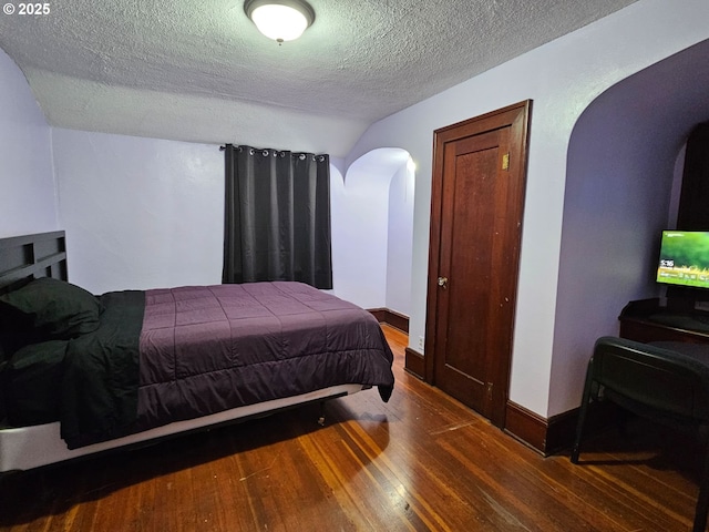 bedroom with arched walkways, hardwood / wood-style floors, a textured ceiling, and baseboards