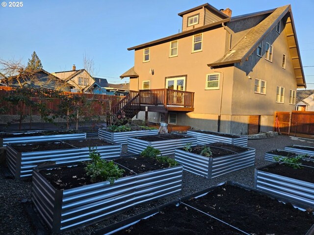 rear view of house with a vegetable garden, fence, and stucco siding